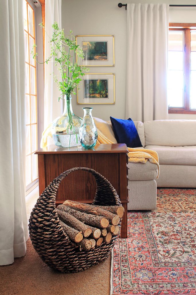 A woven basket containing wooden logs, next to an end table and sofa