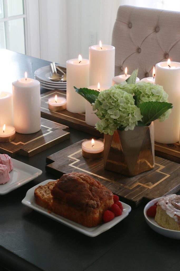 Lit candles on wooden trays with gold leaves and flowers in a vase